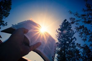 A man holds a bible up to the sun.